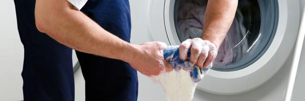 Waschmaschine läuft aus - Mann beim Auswinden eines nassen Lappens vor einer Waschmaschine - Header
